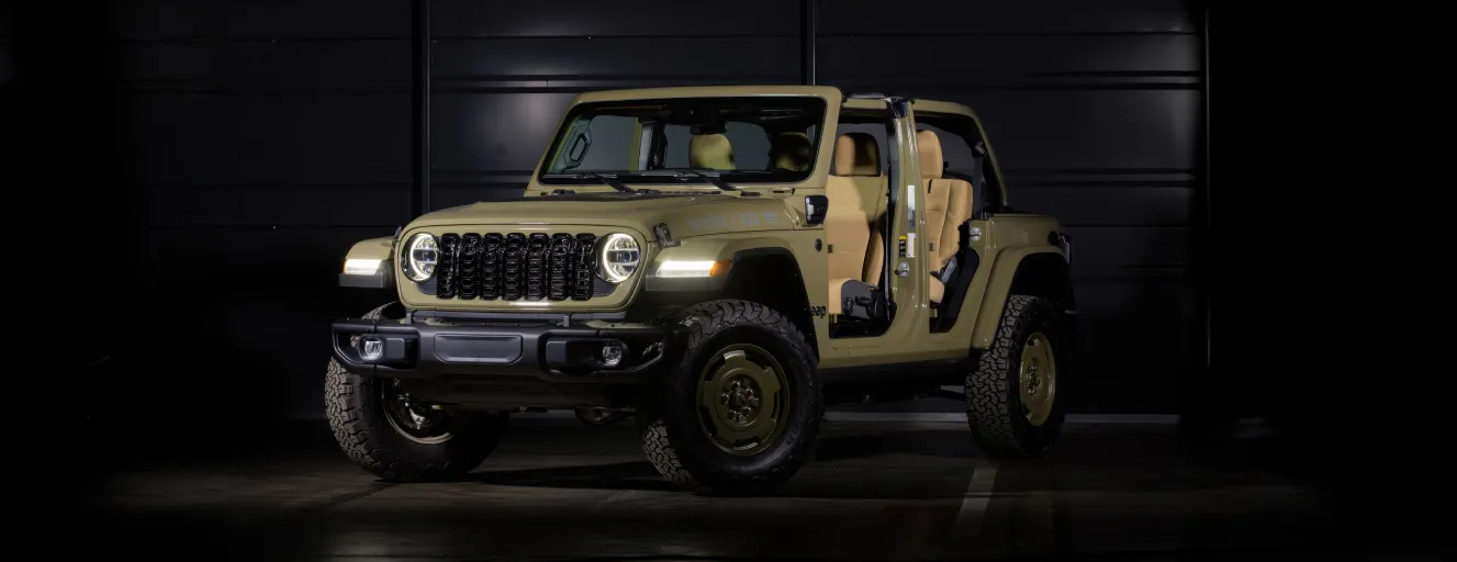 A tan Jeep Wrangler with doors removed, showcasing its rugged interior and off-road tires in a dark studio.